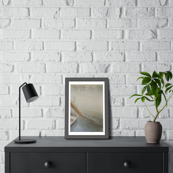 Framed watercolor painting by Veronique Semple depicting a serene lakeside scene with a boat partially visible in soft, misty hues, displayed on a modern black console table. - Bromont Media